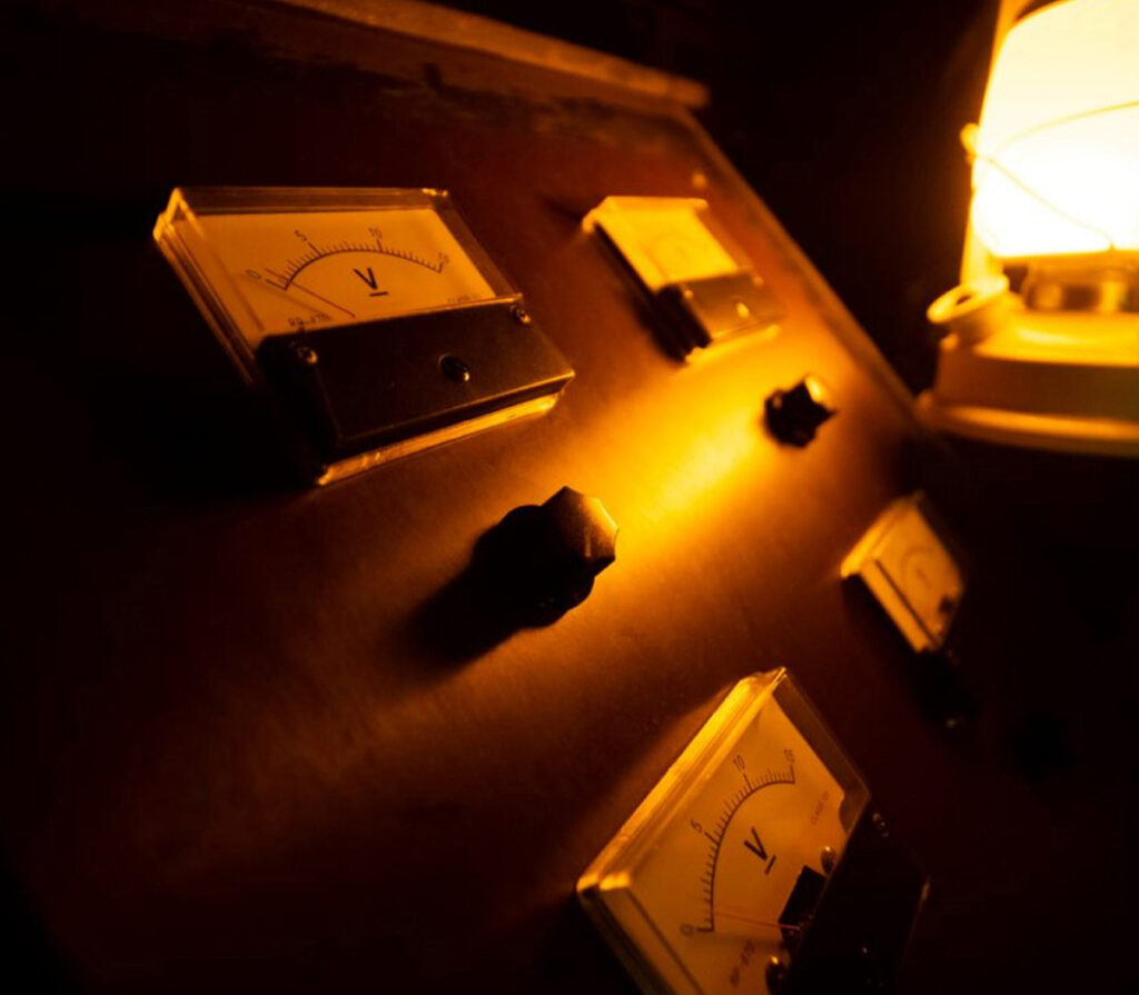 High-voltage electrical meters with glowing orange lighting in an escape room setting.