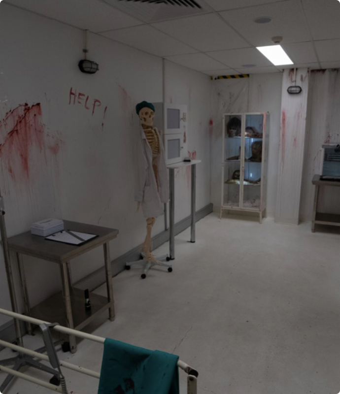 Blood-splattered hospital room with skeleton mannequin, medical equipment, and creepy atmosphere for escape room experience.