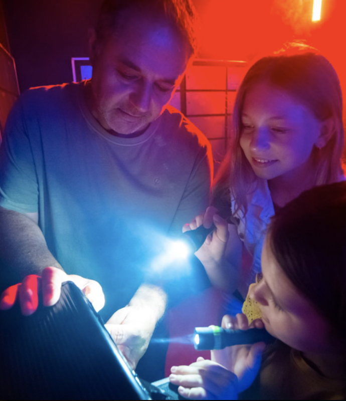 Clue-solving in escape room at Fox in a Box Stockholm with children and adult, illuminated by flashlights.