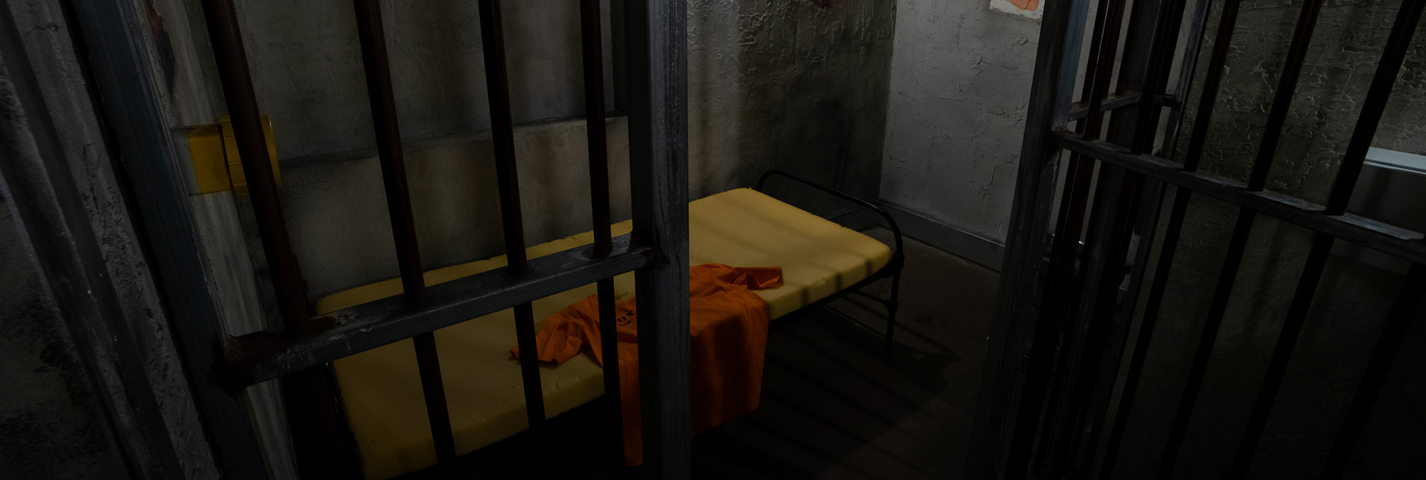 Cell block with metal bars and a yellow bed in an escape room setting, eerie prison-themed decor.