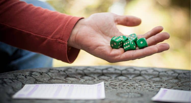 Colorful six-sided dice held in a person’s hand outdoors.